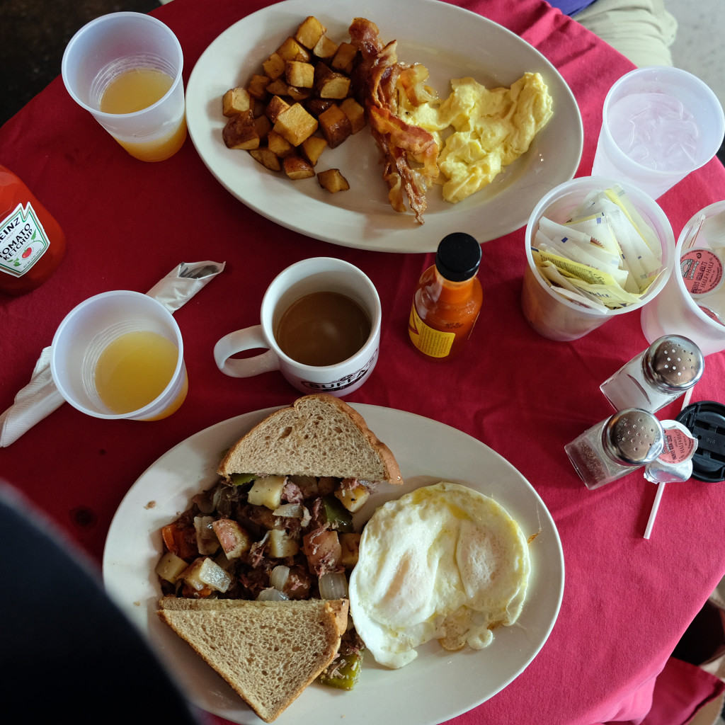 table with breakfast of bacon, eggs, homefries and corned beef hash, with coffee and mimosas